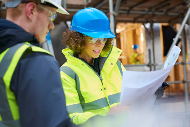 a female construction worker stands on a building site housing development and instructs a co -worker.